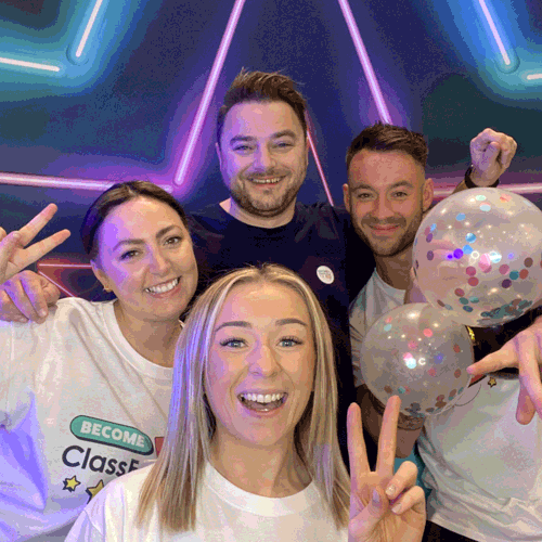 Four smiling members of the ClassForKids team pose in front of a colourful neon star backdrop. They’re wearing branded t-shirts, making peace signs, and holding confetti-filled balloons, clearly enjoying the event atmosphere.