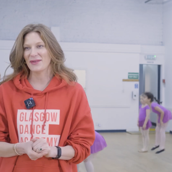 Blonde woman wearing an orange Glasgow Dance Academy hoodie with dancers in the background