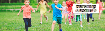 A group of young children run joyfully across a grassy field during a Munchkin Sports session.The children are dressed in bright, colourful clothing, and the Munchkin Sports logo appears in the top right.
