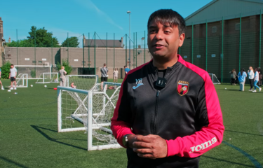 Tots United owner standing on a football pitch with pupils playing in the background
